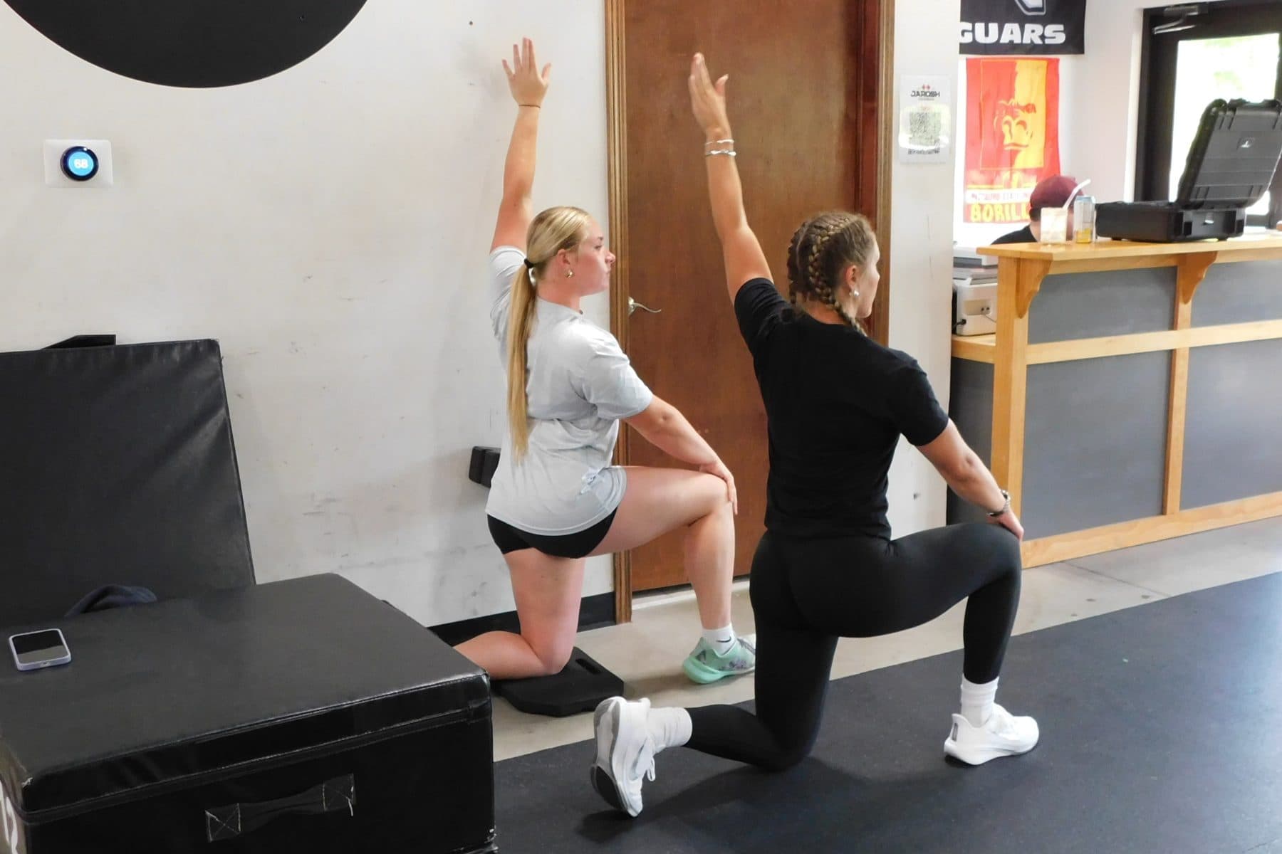 A Jarosh Performance coach demonstrates a half-kneeling reach alongside an athlete.