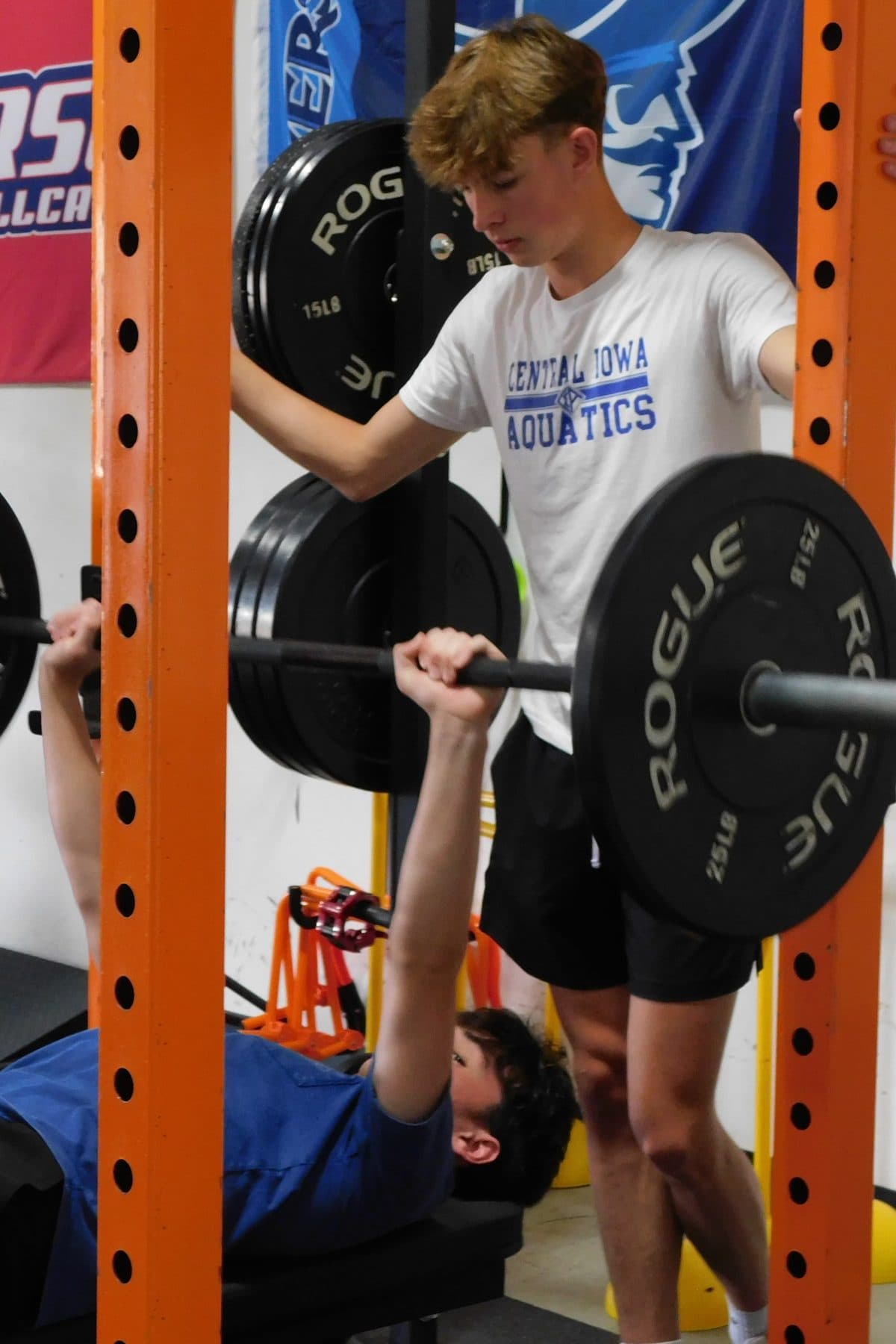 An athlete performs a barbell bench press with a spotter.