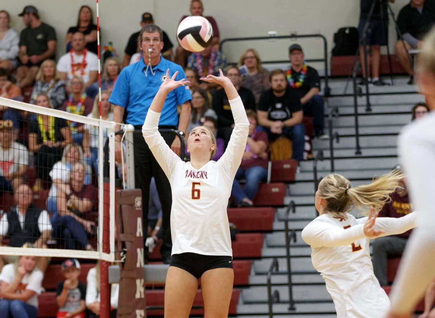 A volleyball setter sets the ball at the net during a match.